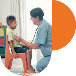 Smiling young black boy sitting on a  chair as female listens to chest with stethoscope