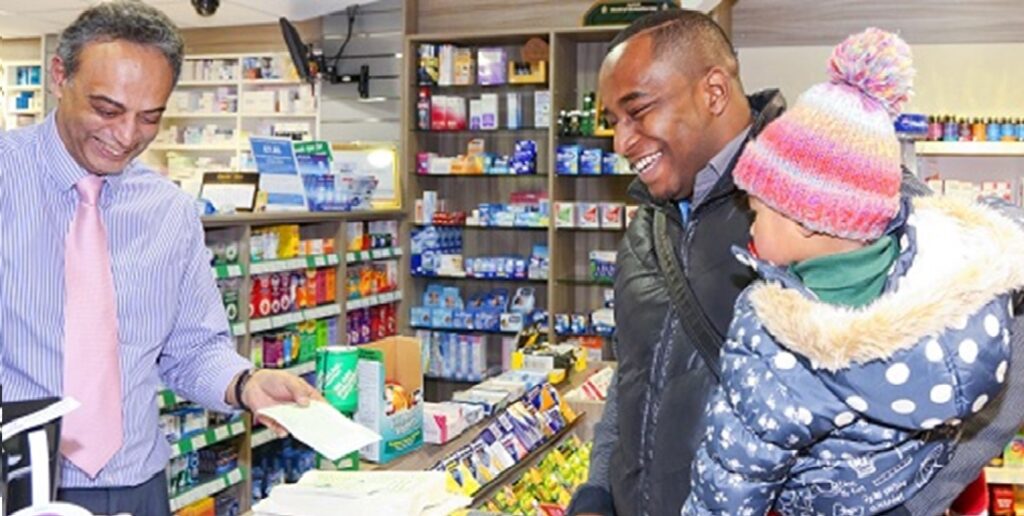 Photo of pharmacist at Cope's Pharmacy serving a young father at the counter, carrying his child.