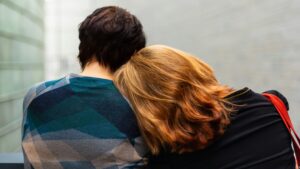 back view of a young couple. The woman sits with her head on her partner's shoulder.