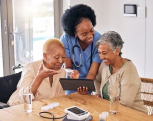 A nurse in the kitchen of a retirement home, showing information on a tablet to two older female friends