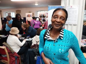 Black woman at health care event, siling, stalls in background