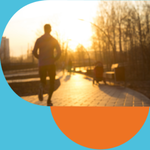  A person jogging along a paved path in a park during sunrise, with trees and benches lining the walkway