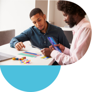 Two people sitting at a table working with colourful cards and blocks, with a laptop nearby.