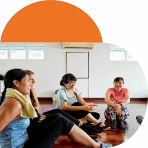 Group of people sitting in a bright yoga studio with wooden floors and large windows, engaged in conversation