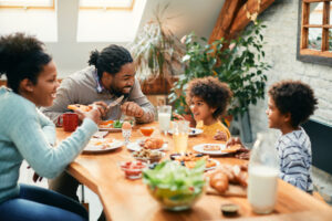 young Black and mixed race family enjoying healthy breakfast together round a table in sunny room